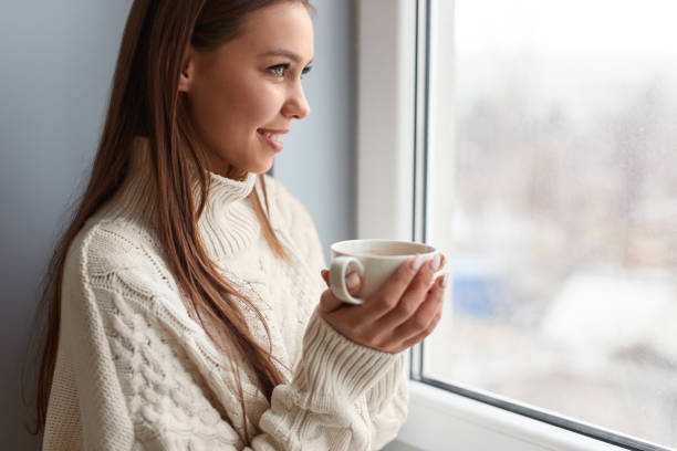 istock Smiling woman with hot coffee near window 1152370534