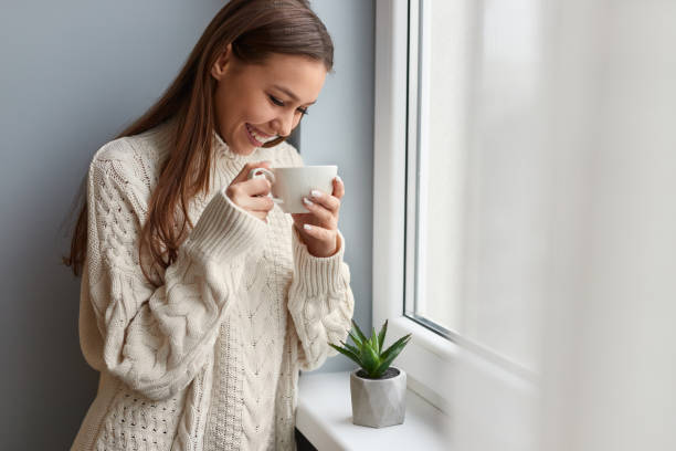 istock Cheerful woman drinking tea near window 1152370563