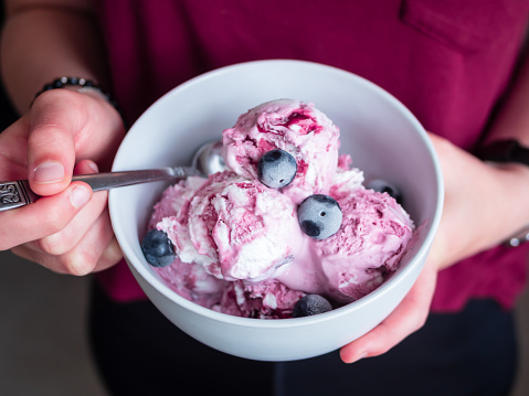 Young woman is holding a white bowl with homemade blueberry ice cream in her hands, top view, eating, spoon, summer