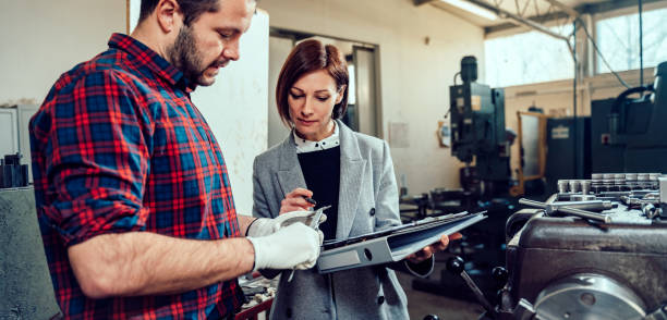 Female engineer consulting with lathe machine operator using caliper Female engineer consulting with lathe machine operator at industrial manufacturing factory micron stock pictures, royalty-free photos & images