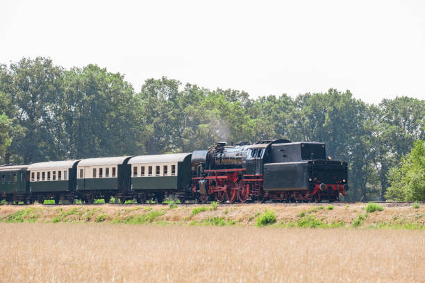 istock Old steam train pulling railway cars driving through the countryside 1152375389