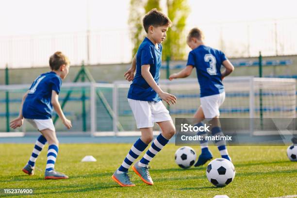 Portrait Of Boy In Junior Youth Football Team Leading Ball Between Cones During Practice In Grass Field Stock Photo - Download Image Now