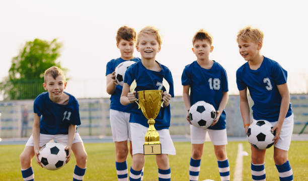 young players of soccer team lift up the golden cup trophy after winning the final soccer match. children celebrate success in sports - youth league imagens e fotografias de stock