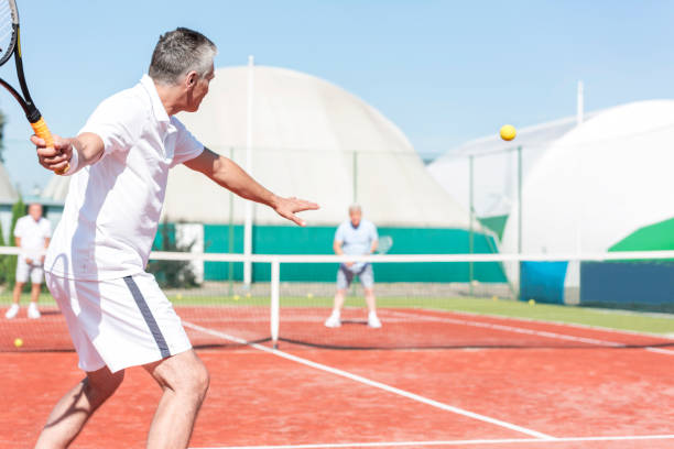 istock Man swinging tennis racket while playing doubles match on red court during summer weekend 1152380302