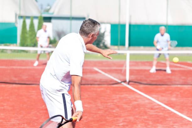 istock Man swinging racket while playing tennis doubles on red court during summer weekend 1152380493