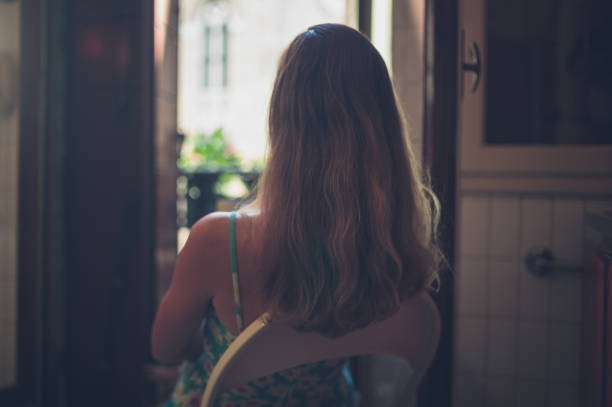 A young woman is sitting in a kitchen by the balcony