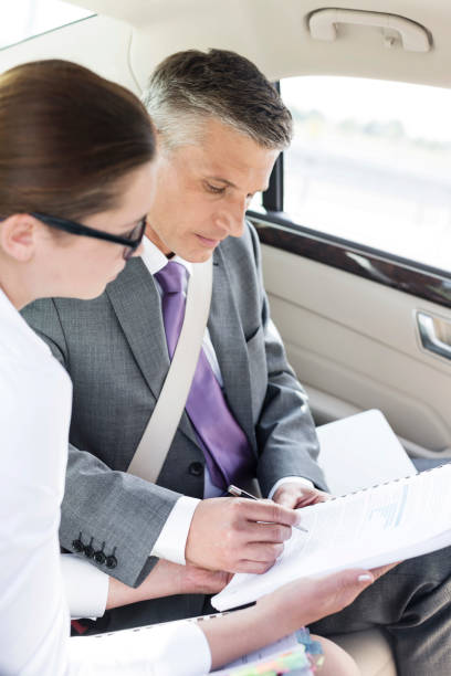 istock Businessman signing documents while sitting by colleague in car 1152384519