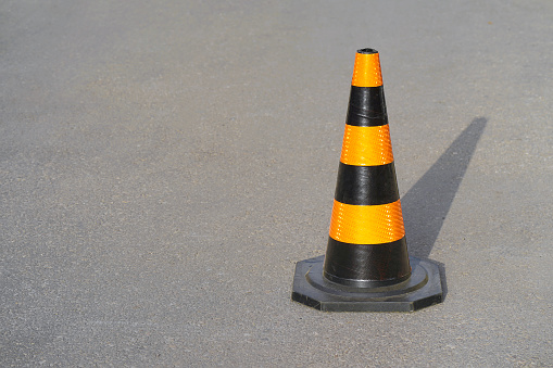 Traffic cone, with black and orange stripes on gray asphalt, copy space. Traffic cone on the road. Road cone on the asphalt.