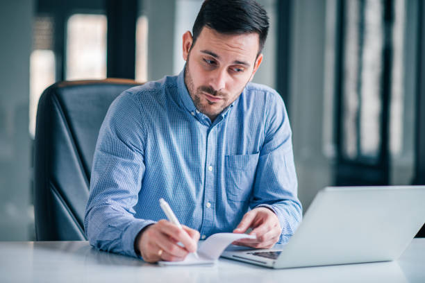 istock Busy man in formal wear writing notes and using laptop. 1152387468