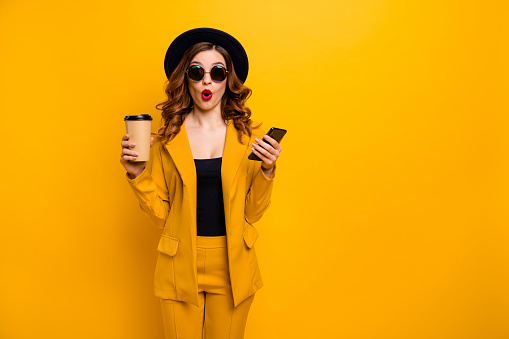 Close up photo beautiful funky she her lady open mouth amazed hands arms telephone vacation traveler hot beverage paper container reader wear specs formal-wear suit isolated yellow bright background.