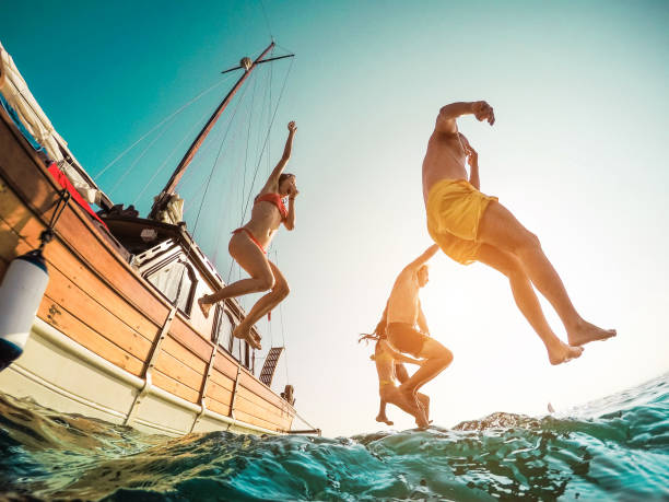 amigos felices buceo de vela en el mar-jóvenes saltando dentro del océano en el día de excursión de verano-vacaciones, juventud y concepto de la diversión-enfoque principal en el hombre de cerca-la distorsión de la lente de ojo de pez - child jumping swimming nautical vessel fotografías e imágenes de stock