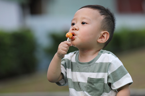 One year old asian boy eats lollipop