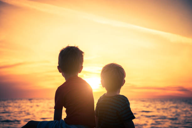 istock Two boys sitting on the rock at the beach at sunset 1152397967