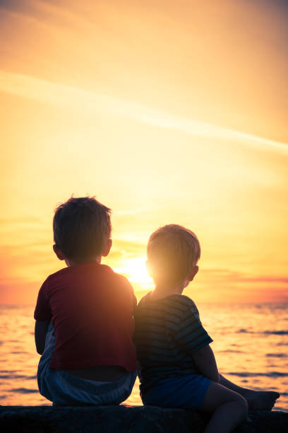 istock Two boys sitting on the rock at the beach at sunset 1152398002