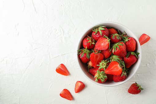 Bowl with fresh strawberries on white background, space for text. Summer sweet fruits and berries