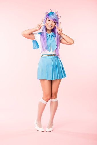 Full length view of cheerful asian otaku girl showing peace signs on pink