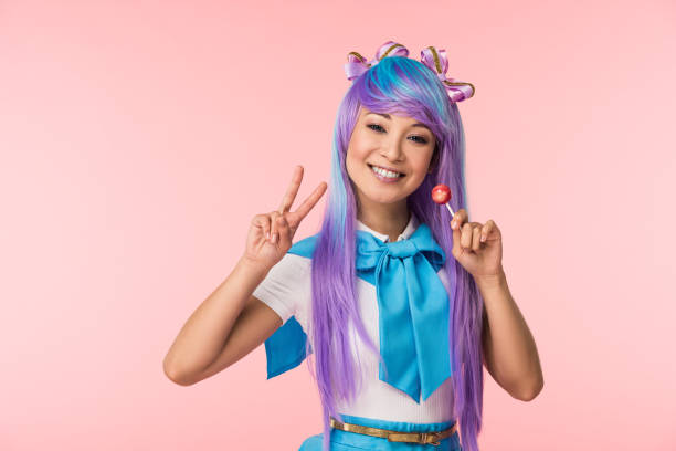 feliz asiática chica anime sosteniendo lollipop y mostrando signo de paz aislado en rosa - cosplay de anime fotografías e imágenes de stock