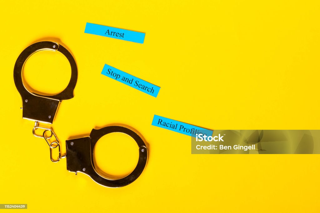 Crime Concept with handcuffs Crime concept showing handcuffs on a yellow background with Racial Profiling Police Force Stock Photo