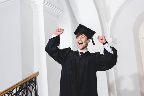 istock happy young man in graduation cap smiling and gesturing in university 1152405296