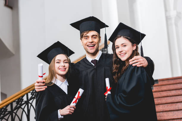 istock cheerful man in graduation cap hugging attractive girls while holding diploma 1152405457