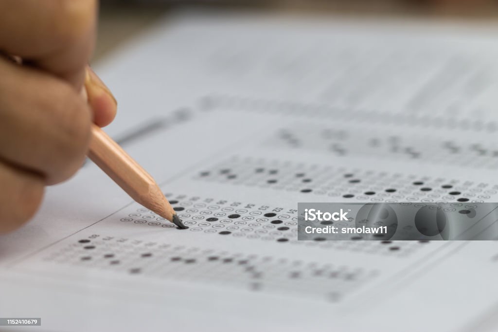 Education school test concept : Hands student holding pencil for testing exams writing answer sheet or exercise for taking fill in admission exam multiple carbon paper computer at university classroom Educational Exam Stock Photo