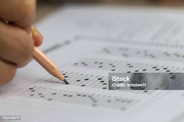 Education School Test Concept Hands Student Holding Pencil For Testing Exams Writing Answer Sheet Or Exercise For Taking Fill In Admission Exam Multiple Carbon Paper Computer At University Classroom Stock Photo - Download Image Now