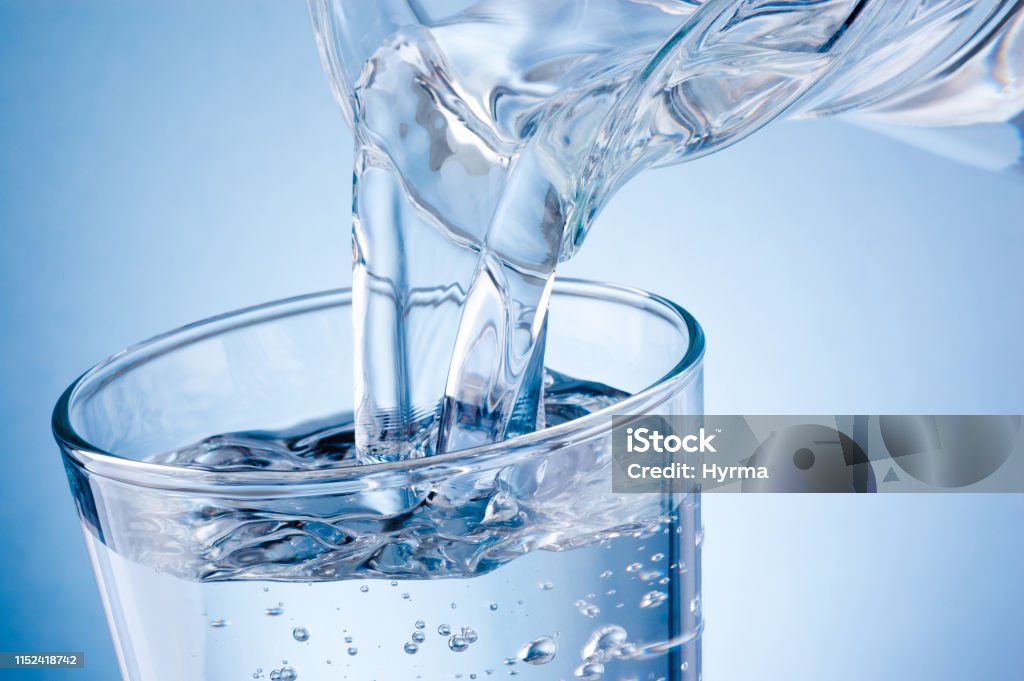 Pouring water from jug into glass on blue background Water Stock Photo
