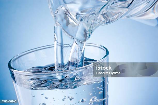 Pouring Water From Jug Into Glass On Blue Background Stock Photo - Download Image Now