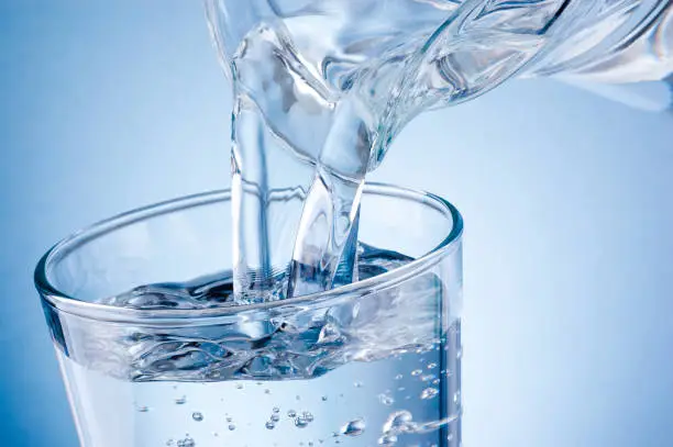 Pouring water from jug into glass on blue background