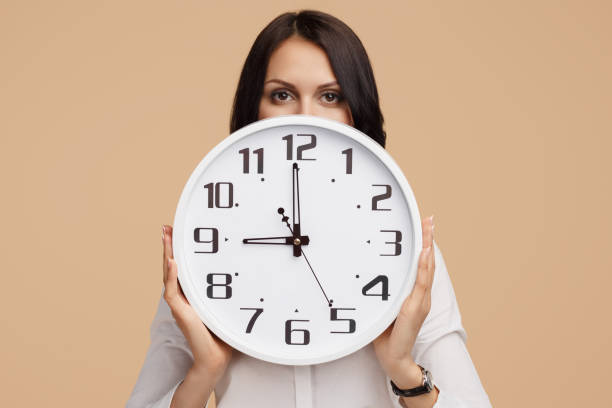 photo of young modern business woman hold a clock in front of the face over beige background. - clock face clock deadline human hand imagens e fotografias de stock