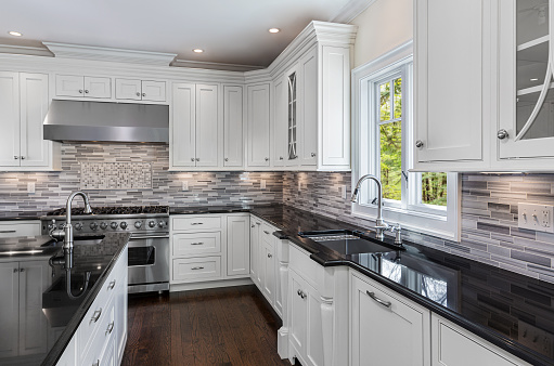 A kitchen detail with white cabinets, gold hardware and faucet, marble countertops, and a brown picket tile backsplash.