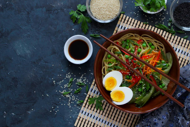 istock Noodles with vegetables and eggs in bowl on dark background. 1152432258