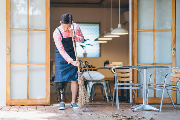 istock Man with artificial leg is sweeping leaves in front of his shop. 1152433311