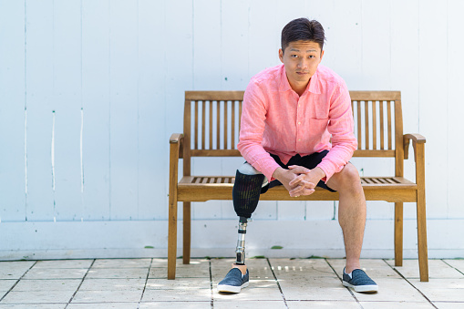 A portrait of a man with a prosthesis leg sitting at a bench.