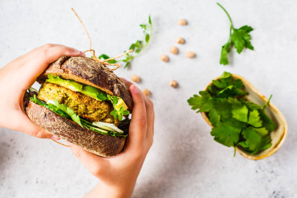 panino vegano con tortino di ceci, avocado, cetriolo e verdure nel pane di segale nelle mani dei bambini. - salad vegetable hamburger burger foto e immagini stock