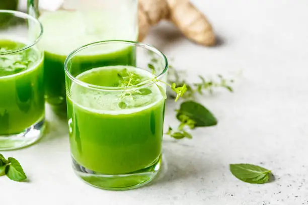 Photo of Green detox juice with ginger and mint in glasses and jars.