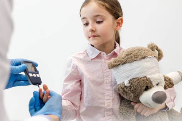 Doctor checking diabetics on equipment of girl with teddybear at clinic stock photo