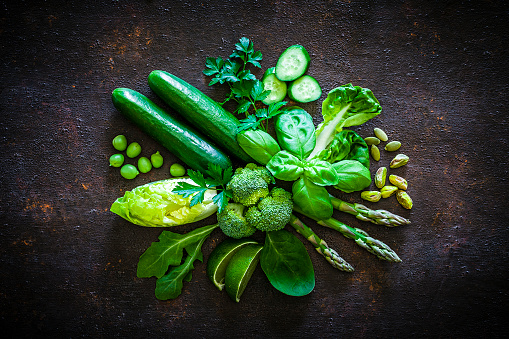 Top view of healthy fresh green vegetables for a detox diet or healthy eating shot on dark rustic table. Vegetables included in the composition are cucumbers, lettuce arugula, green peas, asparagus, broccoli, parsley, basil, lime and pistachios. Predominant color is green. Low key DSRL studio photo taken with Canon EOS 5D Mk II and Canon EF 100mm f/2.8L Macro IS USM.