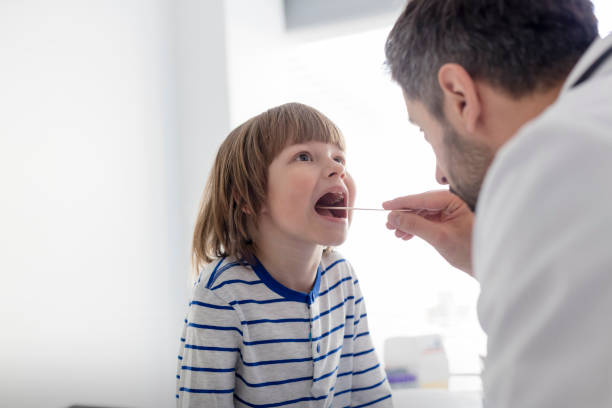 mi pédiatre adulte vérifiant le patient de garçon avec le dépresseur à l’hôpital - doctor patient male tongue depressor photos et images de collection