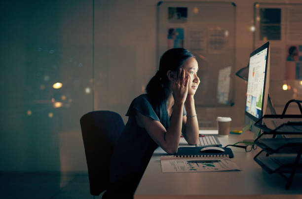 I think it’s time to call it a night Shot of a young businesswoman looking tired while using a computer at night in a modern office staring stock pictures, royalty-free photos & images