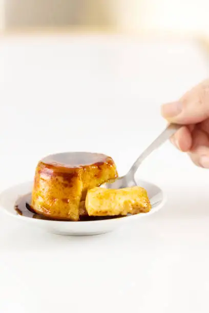 Photo of Creme caramel dessert or flan on white table. Hand holding a piece of delicious flan.