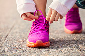 Hands of young woman lacing pink sneakers