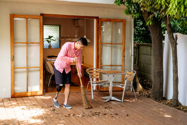 Man with artificial leg sweeping leaves in back yard
