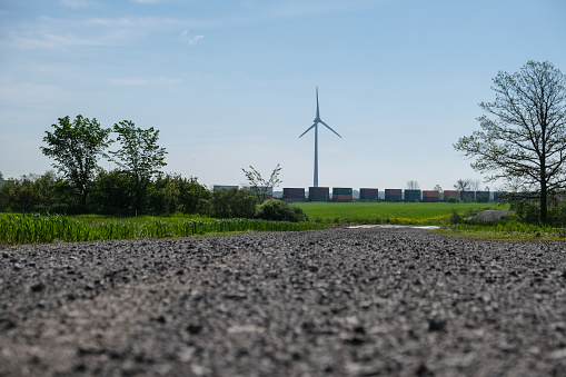 View of a ground road with a train passing through a plantation on a farm and seeing a wind turbine