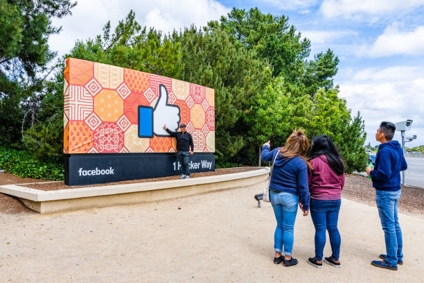 May 26, 2019 Menlo Park / CA / USA - Tourists posing in front of the Facebook Like Button sign located at the entrance to the company's main headquarters located in Silicon Valley (1 Hacker Way);