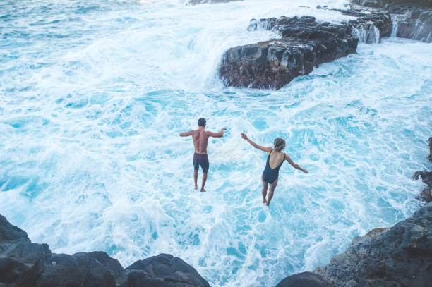 istock Couple jumping off a rocky cliff into the ocean for fun 1152466496