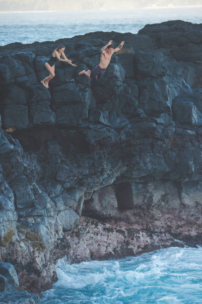 istock Couple jumping off a rocky cliff into the ocean for fun 1152466499
