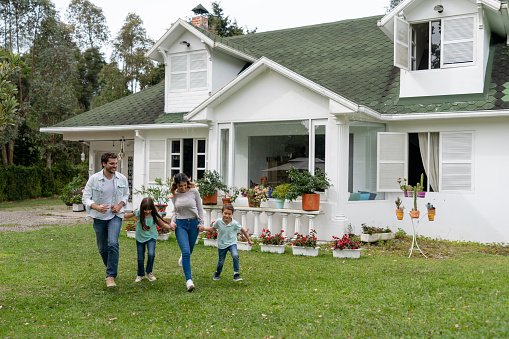 Happy Latin American family playing outside their house running and smiling - real estate concepts