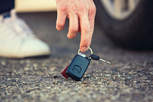 Cierre de las llaves del coche de levantamiento de mano del hombre caído en el suelo. El tipo encontró las llaves del vehículo que alguien perdió en la carretera asfaltada en el estacionamiento. photo