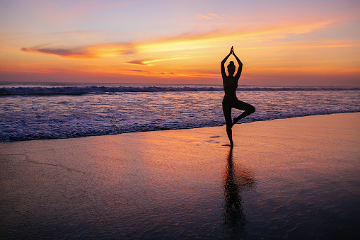 silhouette of a woman practicing yoga on the Bali beach in the early morning or a sunset hour.